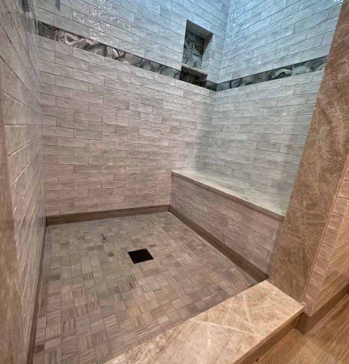 Glossy ceramic tile installed for bathroom wall with a darker tile accent and a basketweave tile installed for the flooring
