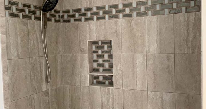 Marble tiled shower wall accentuated with dark-colored tile border and shower niche
