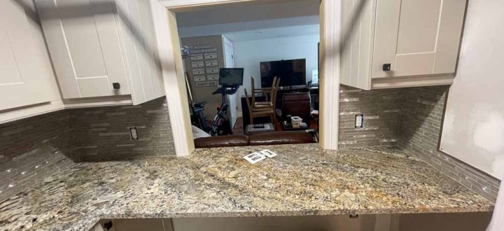 A kitchen with a countertop made of granite and a porcelain tiled backsplash