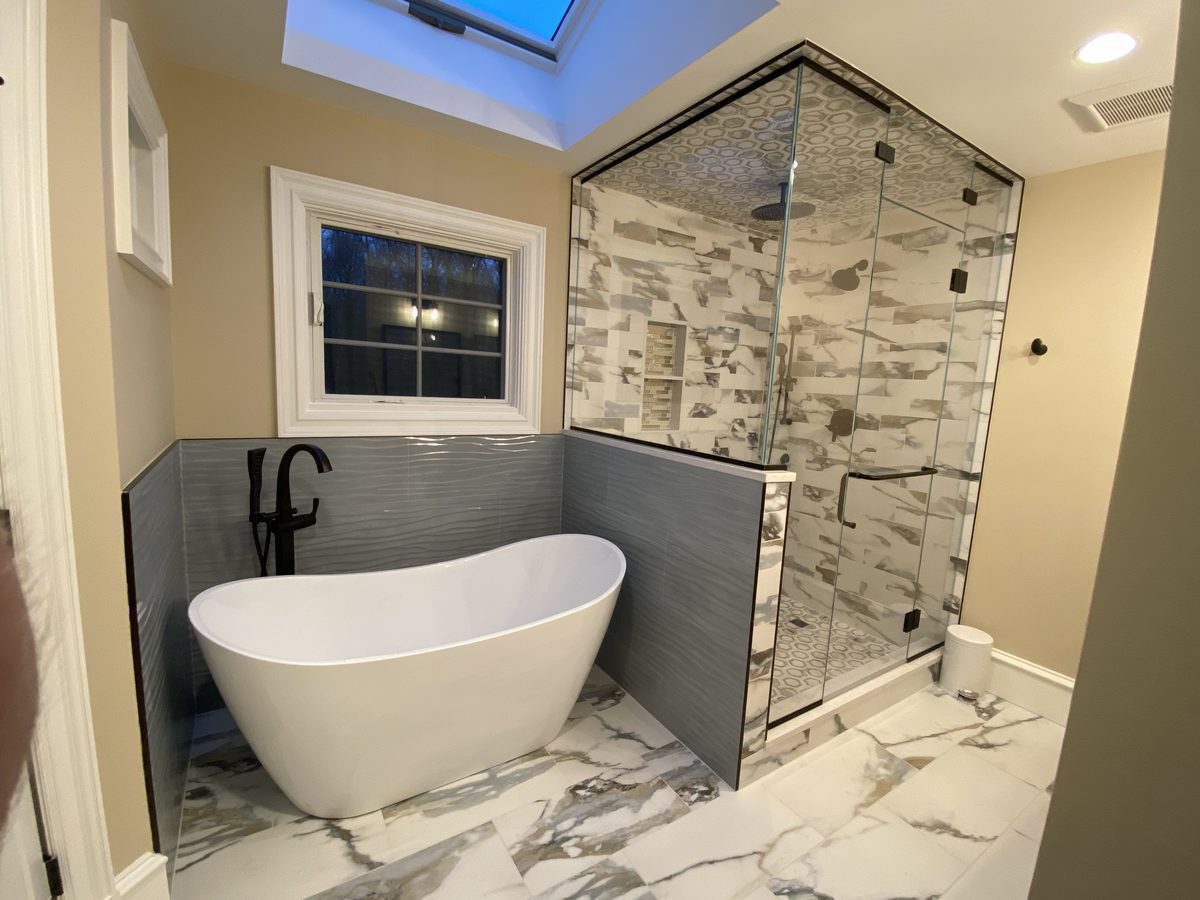 Finished bathroom with a freestanding tub, textured grey wall tile and a glass enclosed corner shower in marble look tile with a hex mosaic ceiling
