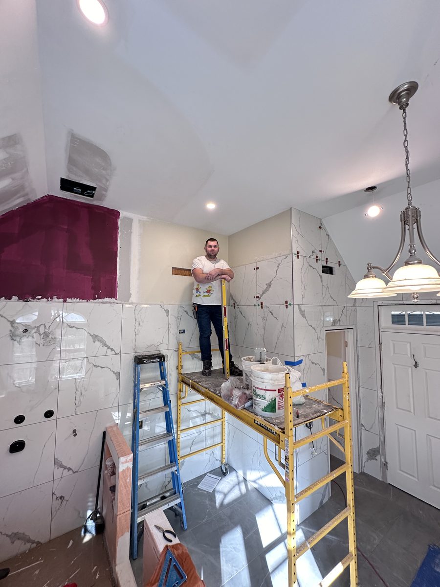 Magic of Tiles installer on a rolling scaffold setting large format marble look wall tile, with levelling clips along the tile edges
