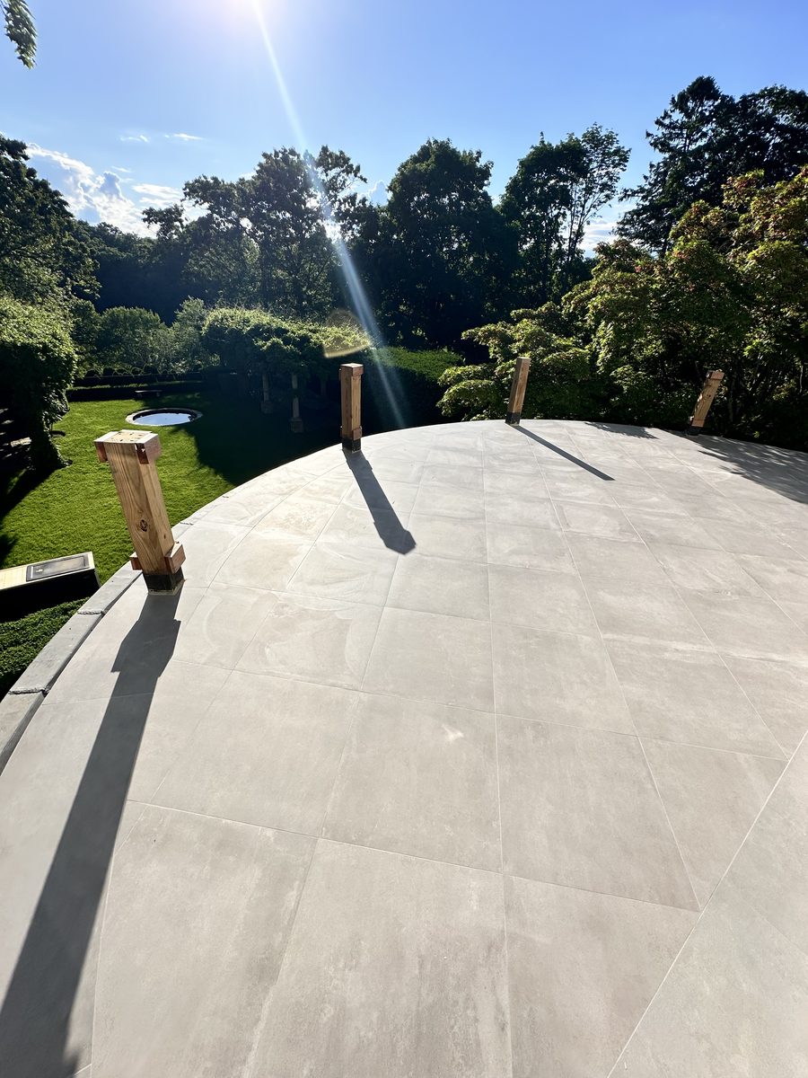 Large format porcelain paving on a curved outdoor terrace, with lawn and mature trees beyond