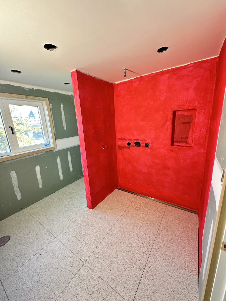 Shower alcove coated in red liquid waterproofing membrane with a formed niche and a linear drain, photographed before tile goes on